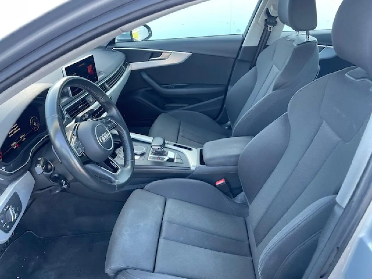 Intérieur avant de l'Audi A4 2019 en tissu gris avec volant multifonction et console centrale argentée vue côté conducteur.