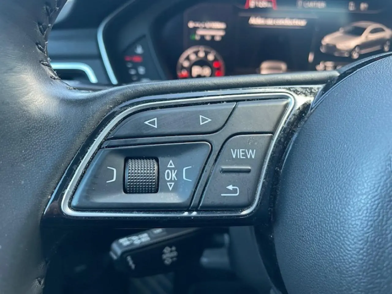 Gros plan sur les commandes multifonctions à gauche du volant cuir noir de l'Audi A4 argent Fleuret Metal 2019.