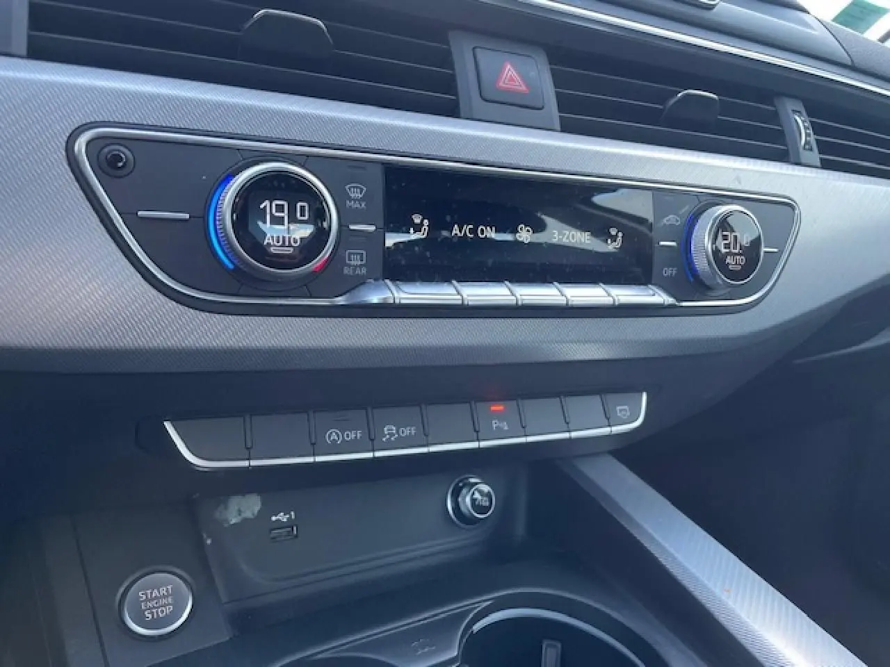 Tableau de bord argenté de l'Audi A4 2019 avec commandes climatisation 3 zones et boutons multifonctions au centre