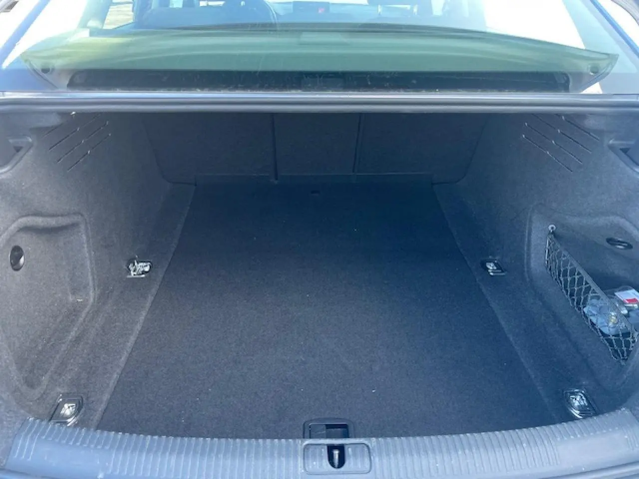 Coffre ouvert d'une Audi A4 argent fleuret métal, montrant les quatre œilletons de fixation et un filet de rangement latéral.