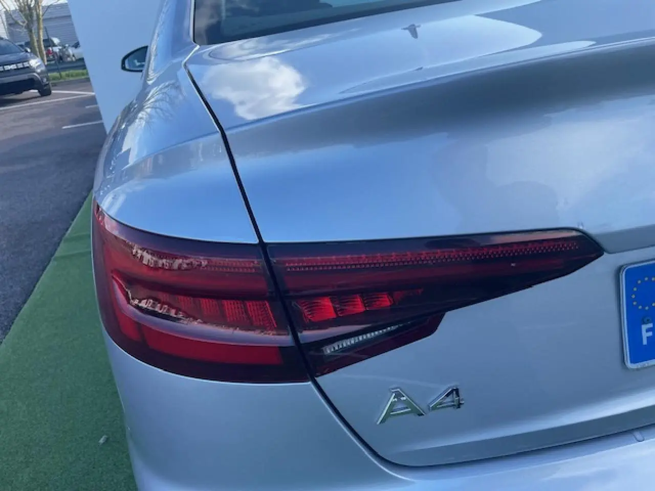 Gros plan sur le feu arrière gauche d'une Audi A4 argent fleuret métal avec logo A4 visible sur le coffre.