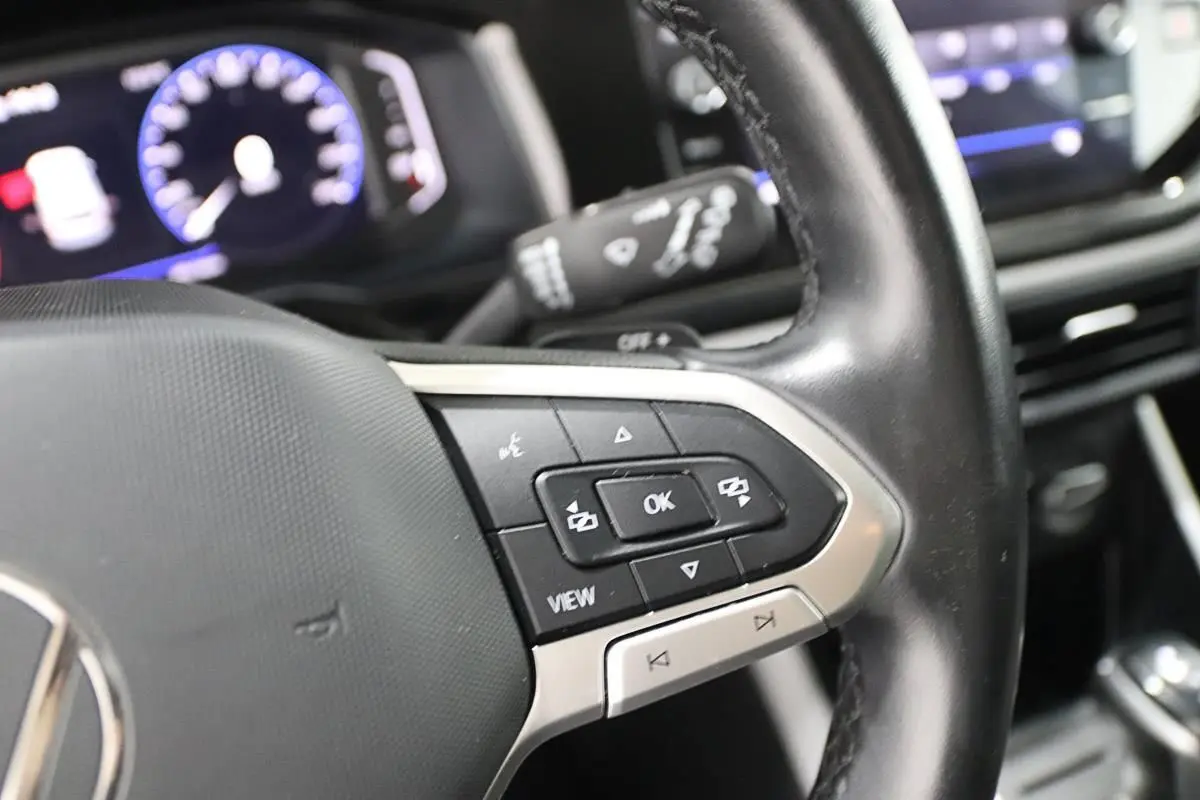 Gros plan sur le volant noir de la Volkswagen Polo 2022 avec commandes multifonctions et affichage digital du tableau de bord flou.