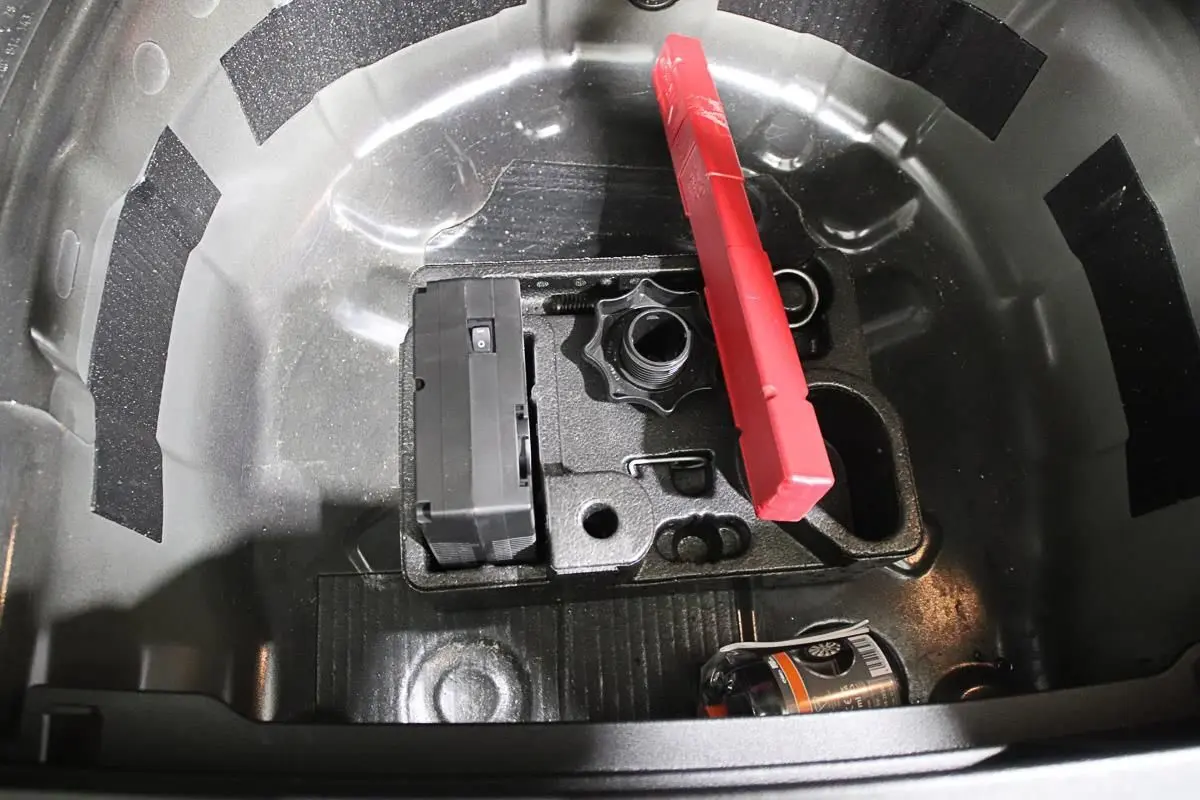 Coffre ouvert montrant le rangement sous plancher avec kit de réparation pneus et triangle de signalisation rouge.