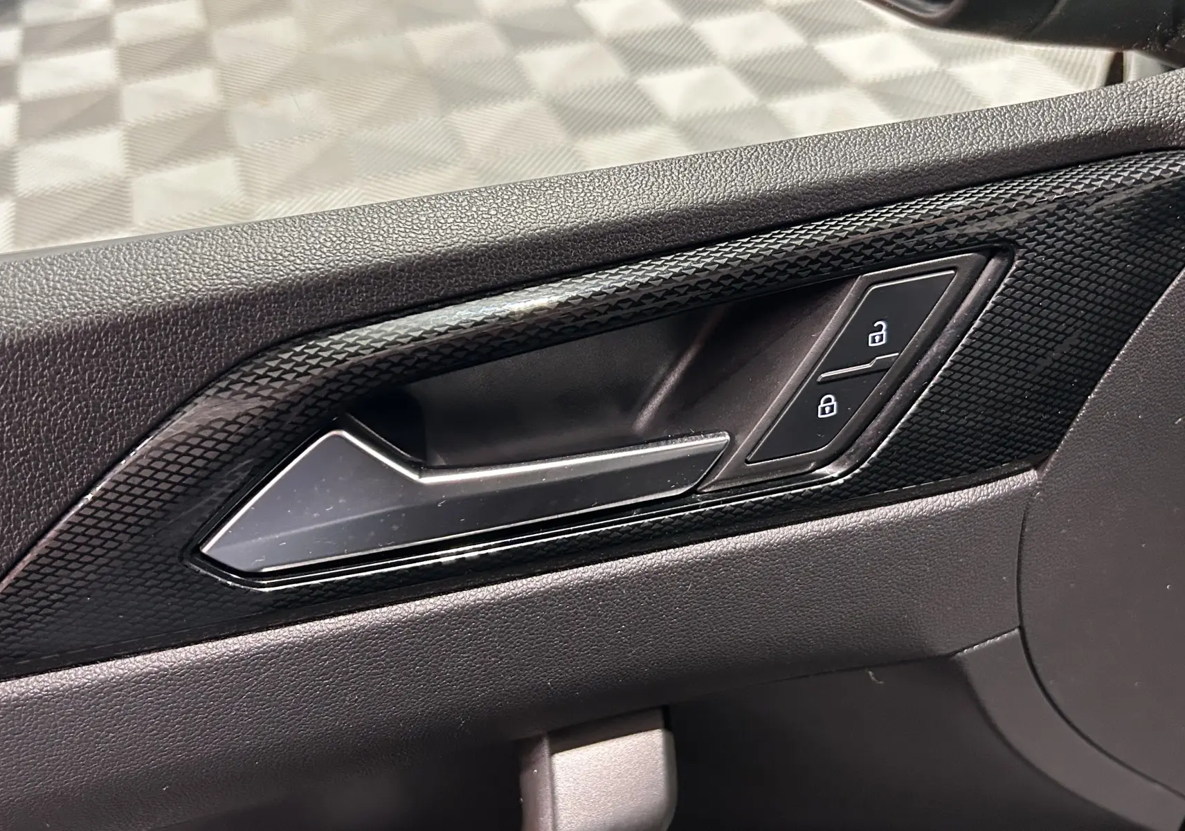 Gros plan sur la poignée intérieure côté gauche de la porte noire avec boutons de verrouillage déverrouillage.