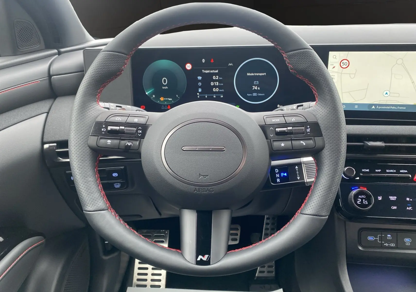 Vue frontale du volant cuir noir avec surpiqûres rouges du Hyundai Tucson 2026, tableau de bord digital et écran GPS visibles.