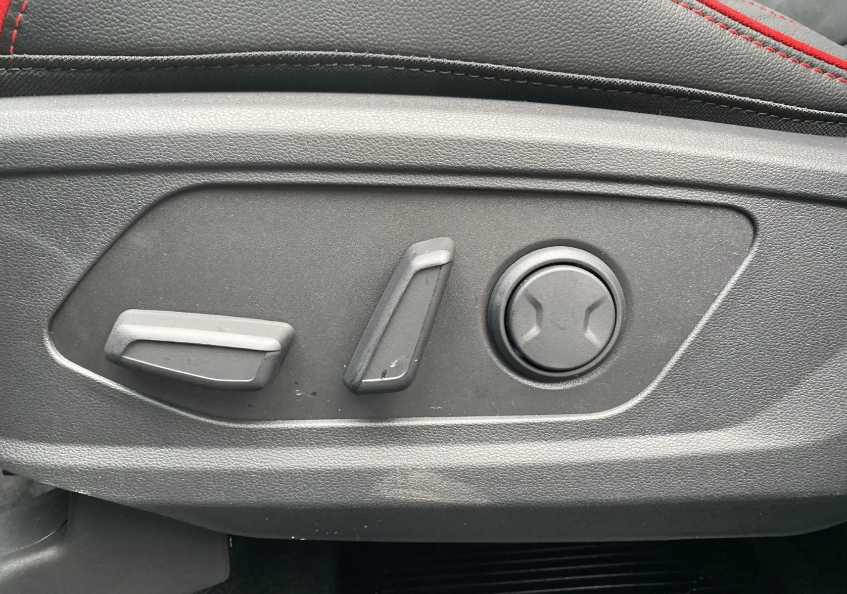 Gros plan sur les commandes de réglage électrique du siège conducteur du Hyundai Tucson 2026 en cuir noir avec surpiqûres rouges.