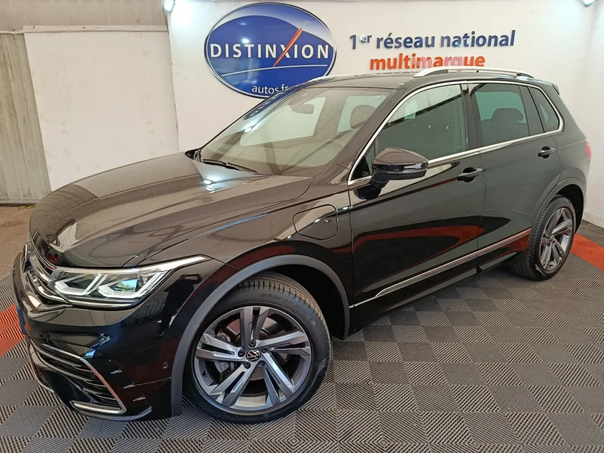 Vue 3/4 avant droit du Volkswagen Tiguan 1.4 eHybrid noir avec jantes alliage et détails R-Line en showroom.