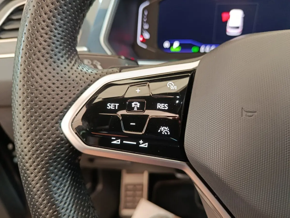 Gros plan sur le volant noir perforé du Volkswagen Tiguan 2023, avec commandes de régulateur adaptatif visibles.