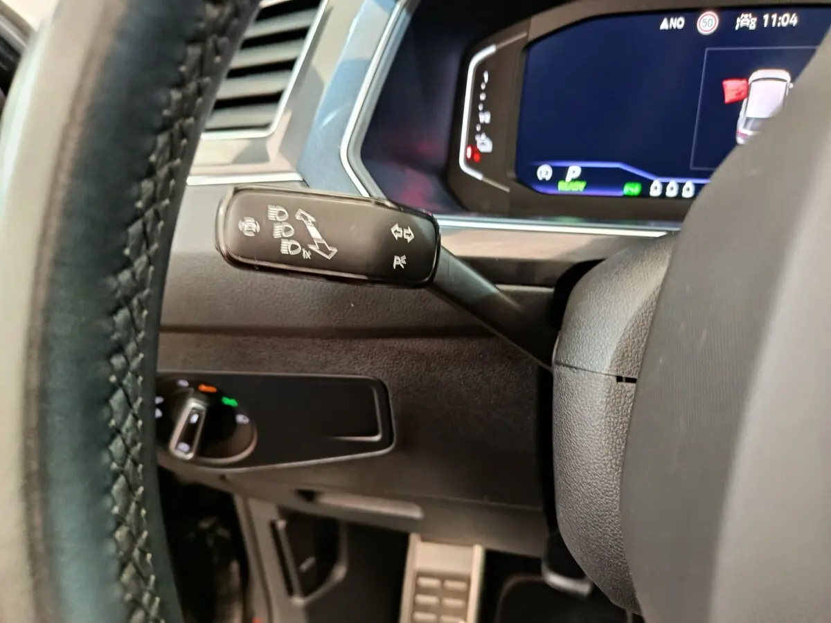 Vue rapprochée du commodo de clignotant et tableau de bord numérique du Volkswagen Tiguan noir 2023 hybride rechargeable.