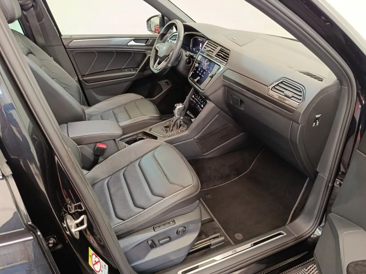 Vue intérieure côté conducteur du Volkswagen Tiguan noir 1.4 eHybrid 2023 avec sièges cuir et tableau de bord digital.