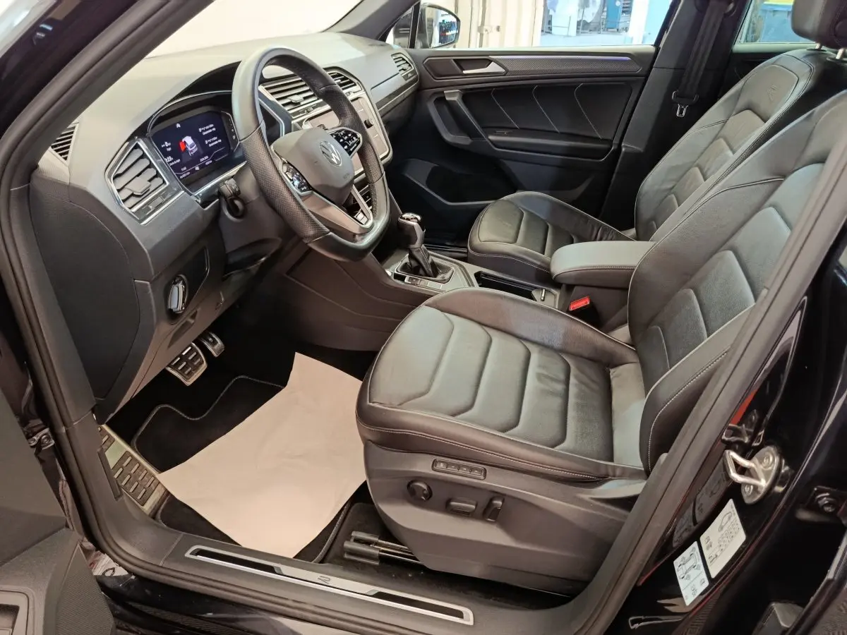 Intérieur avant droit du Volkswagen Tiguan noir 2023, sièges cuir et tableau de bord digital avec volant multifonctions.