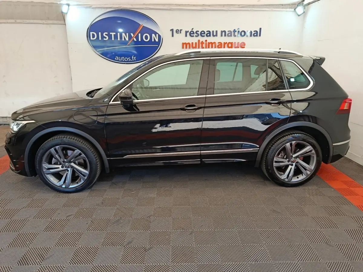 Vue de profil côté gauche du Volkswagen Tiguan noir 1.4 eHybrid 245 DSG6 R-Line Exclusive 2023 en intérieur showroom.