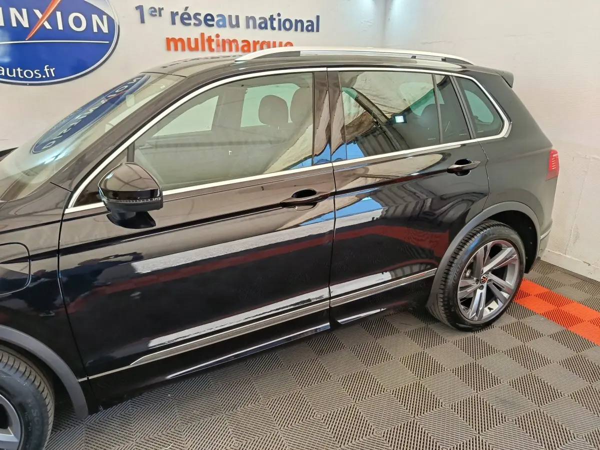 Vue latérale droite du Volkswagen Tiguan noir 2023 avec jantes alliage et rétroviseurs électriques dans un showroom.