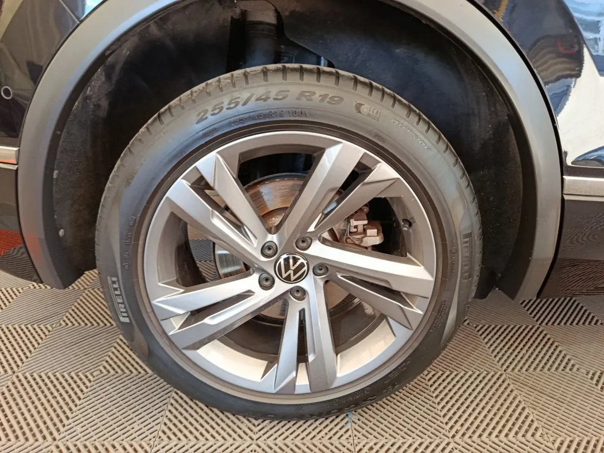 Gros plan sur la roue avant droite du Volkswagen Tiguan noir, mettant en valeur la jante alliage et le logo VW central.