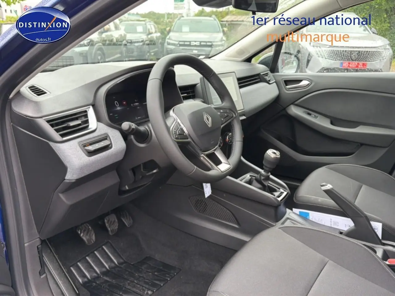 Intérieur de Renault Clio V bleu iron, vue côté conducteur, volant multifonction et boîte manuelle visibles.