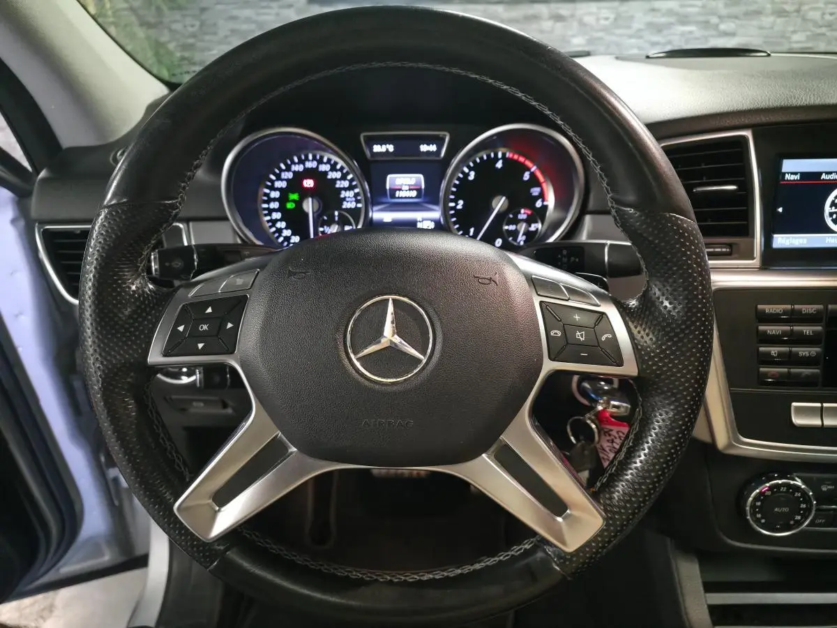 Vue intérieure centrée sur le volant cuir noir perforé et le tableau de bord du Mercedes Classe M gris, 2014.