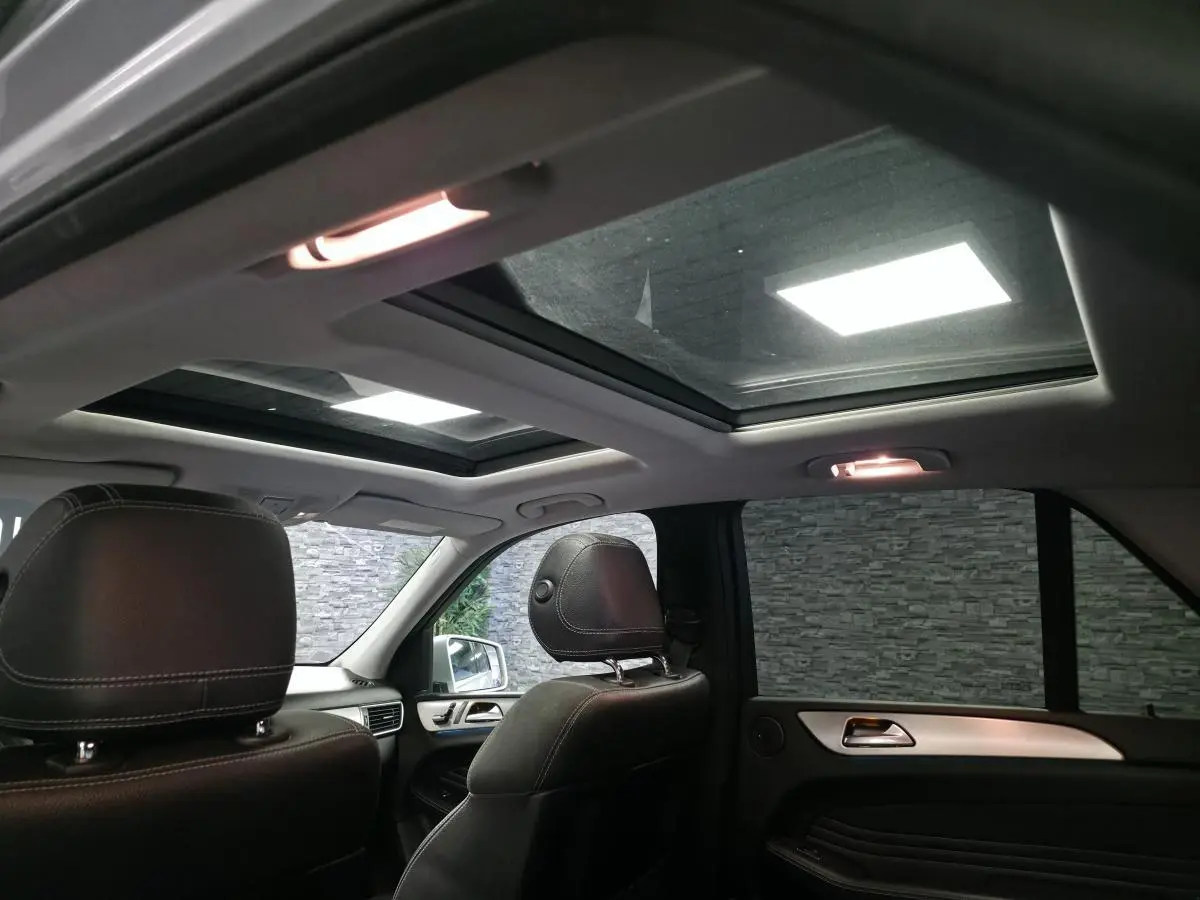 Vue intérieure arrière du Mercedes Classe M gris, mettant en valeur le toit ouvrant panoramique en verre et les sièges cuir noirs.