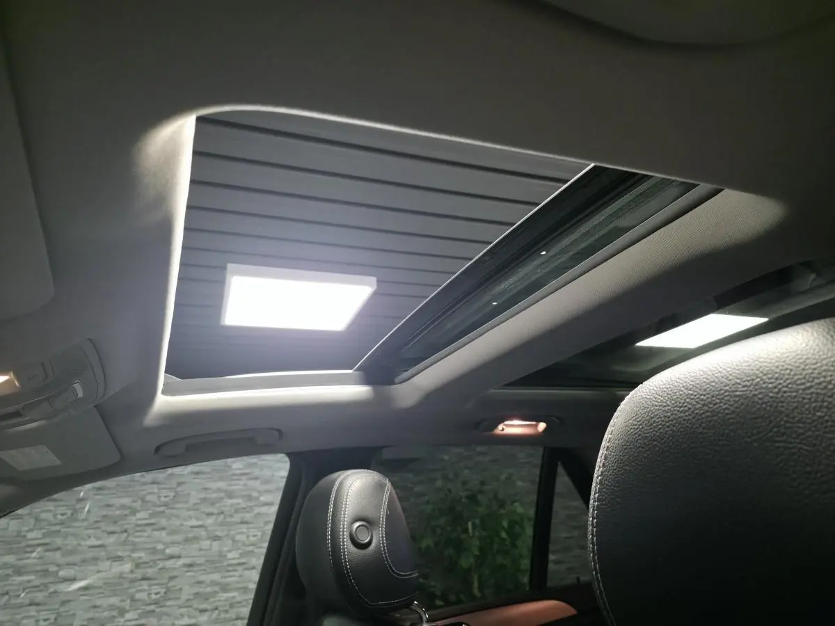Vue intérieure du toit ouvrant panoramique électrique en verre du Mercedes Classe M gris, avec sièges en cuir noir visibles.