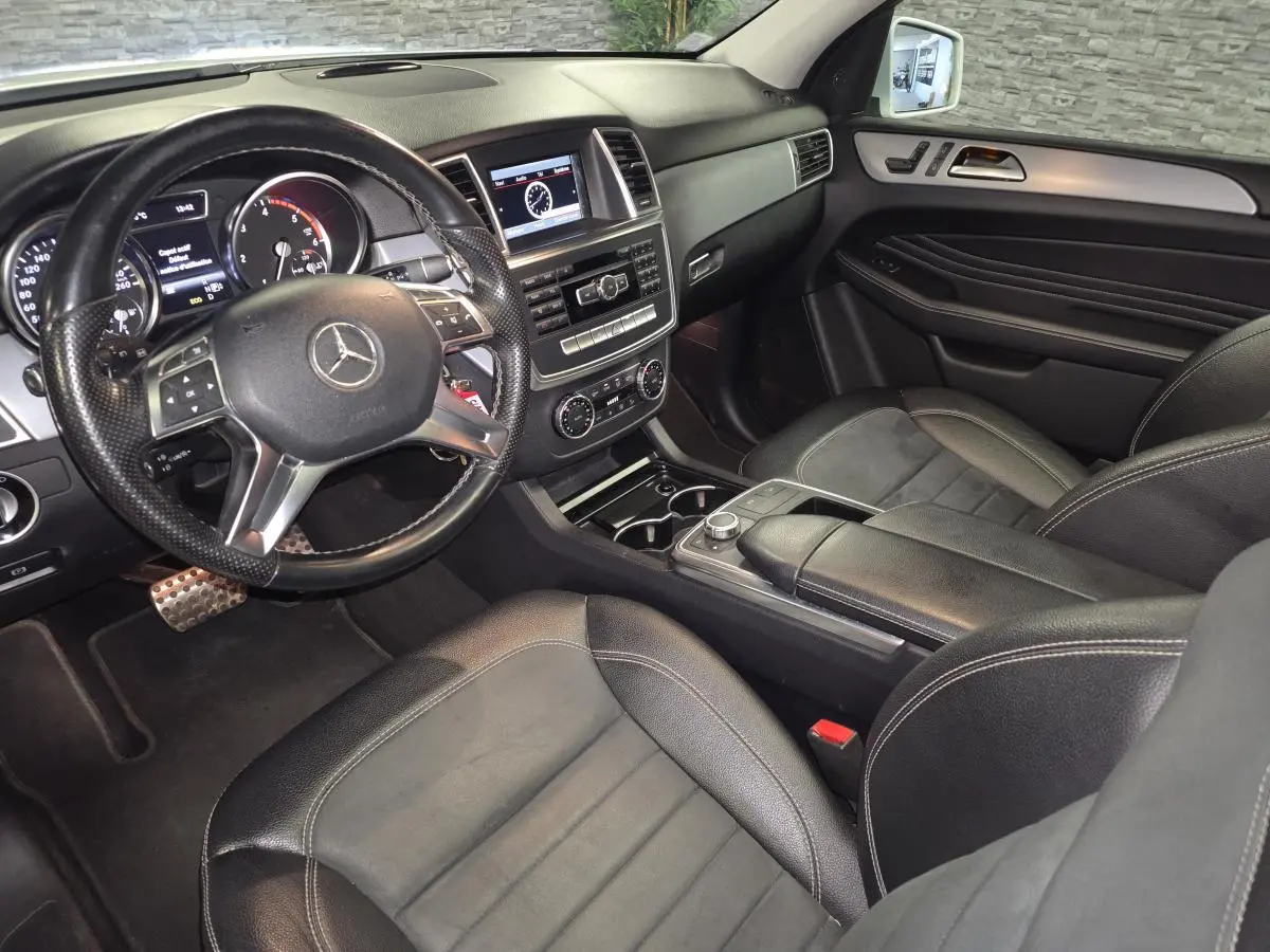 Vue intérieure côté conducteur de la Mercedes Classe M ML 350 BlueTEC 2014 avec tableau de bord noir et volant cuir perforé.