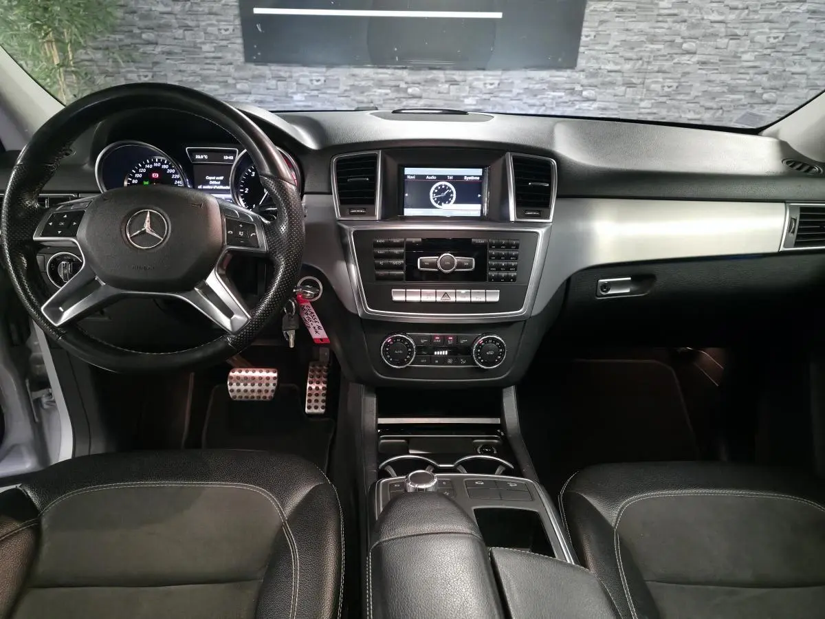 Vue intérieure avant de la Mercedes Classe M 350 BlueTEC 2014, tableau de bord noir avec volant cuir multifonctions et écran central.