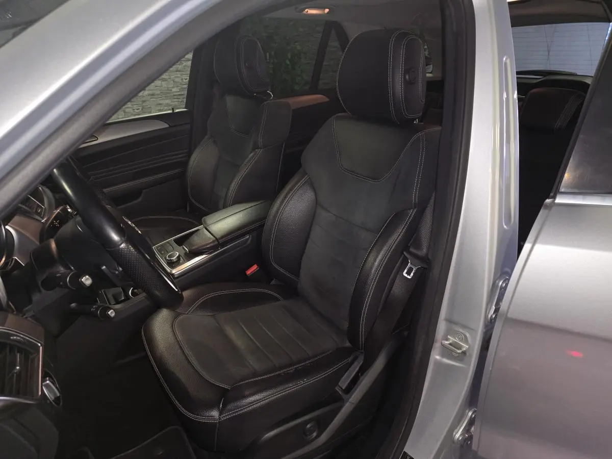 Vue intérieure côté conducteur du Mercedes Classe M gris, sièges en cuir noir avec surpiqûres blanches et console centrale.