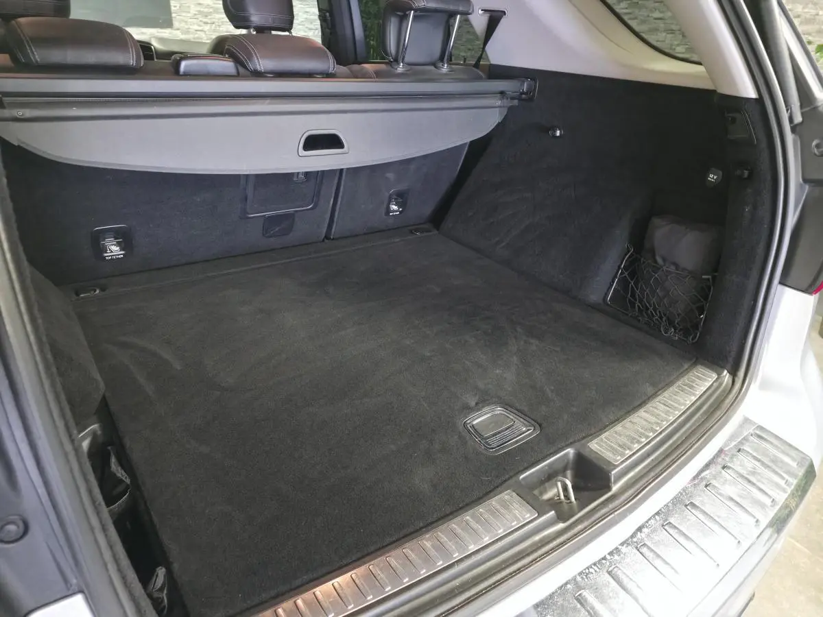 Coffre ouvert vu de l'arrière d'un Mercedes Classe M gris avec cache-bagages et tapis noir.