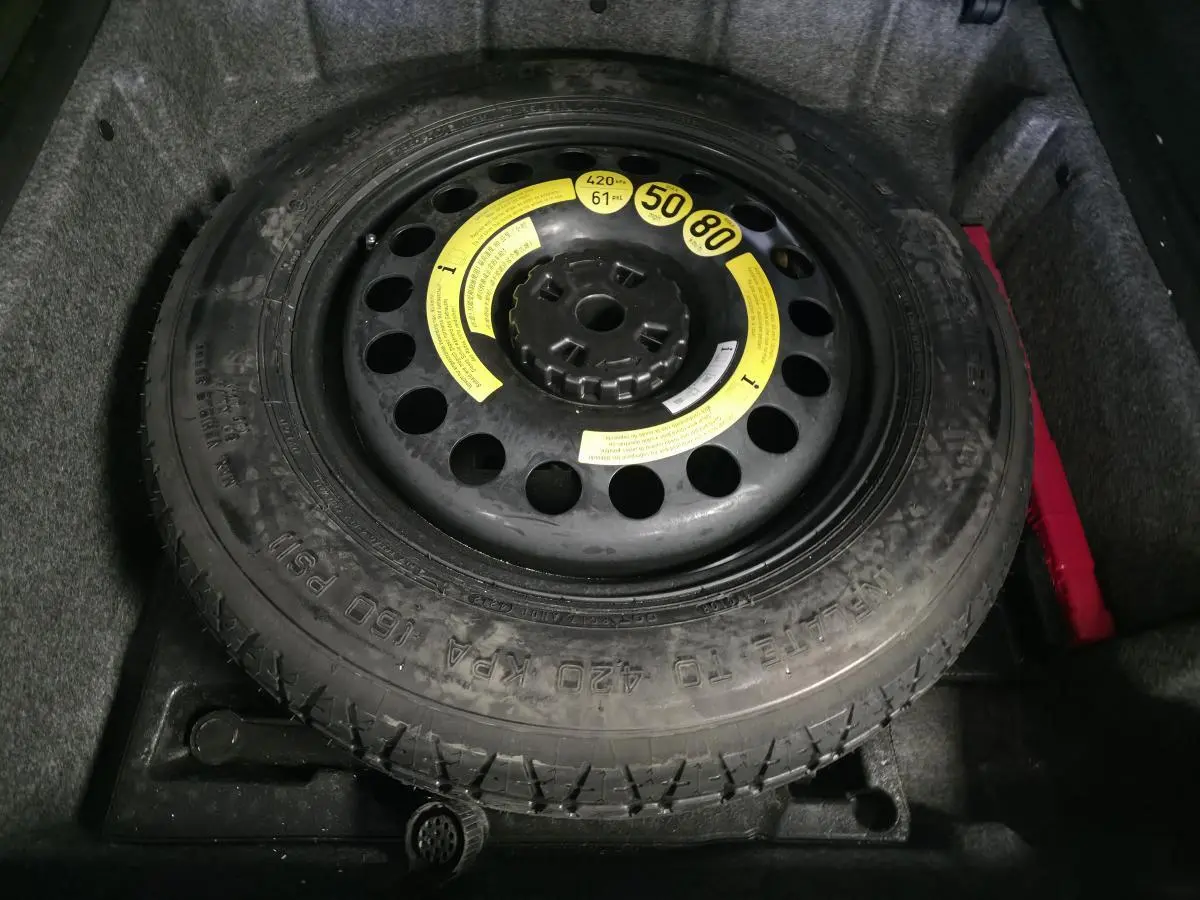 Gros plan sur la roue de secours galette noire dans le coffre d’un Mercedes Classe M gris.