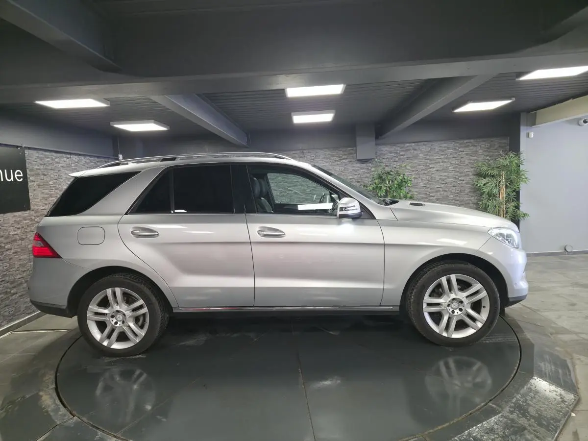 Vue de profil côté gauche d’un Mercedes Classe M gris métallisé avec jantes alliage 5 branches doubles et vitres teintées.