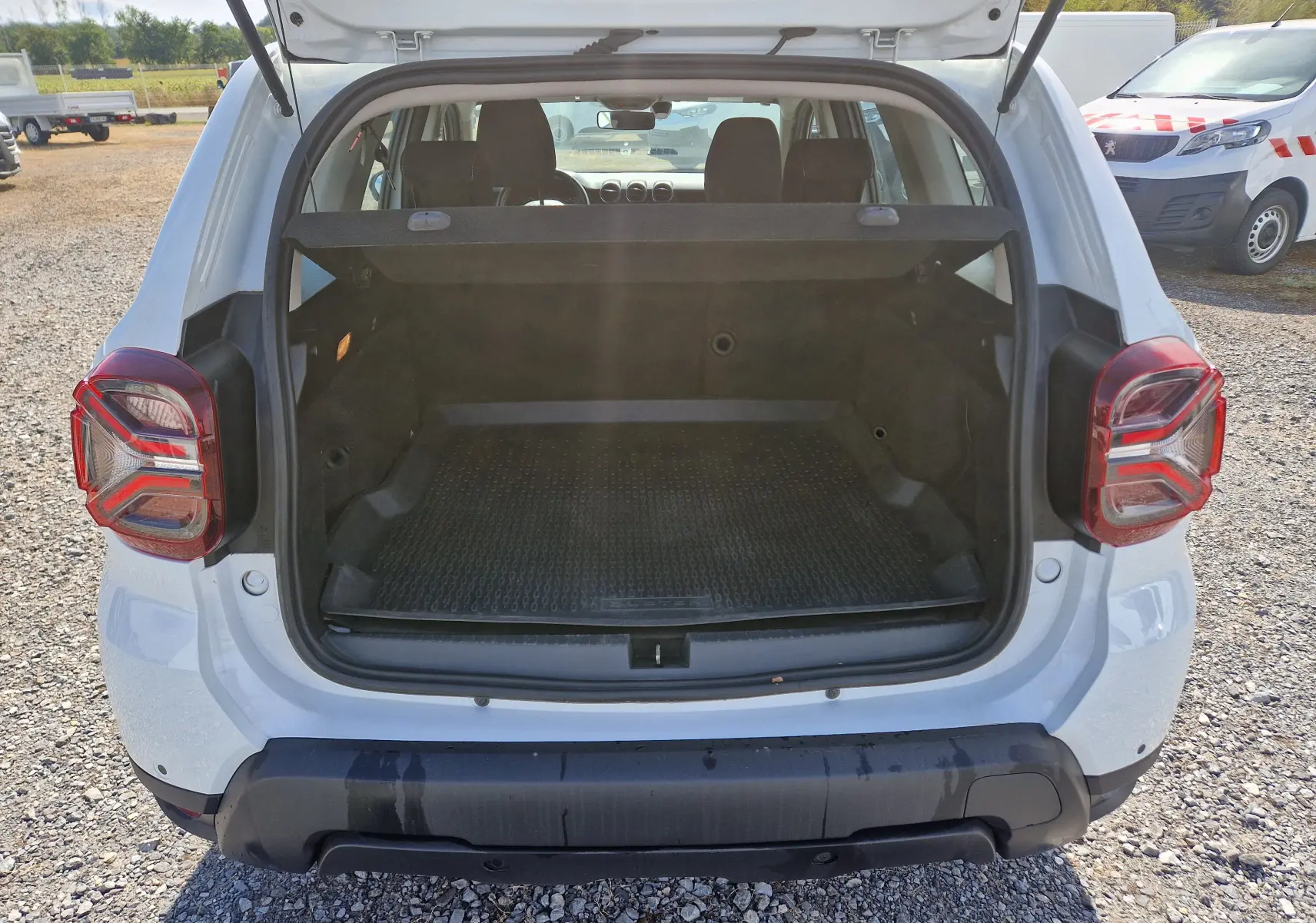 Vue arrière du coffre ouvert d'un Dacia Duster blanc 2023, montrant l'espace de chargement et les feux arrière distinctifs.