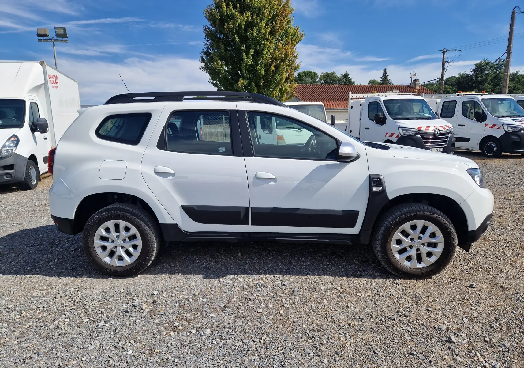 Profil côté gauche d'un Dacia Duster blanc 4x4 2023 avec protections noires et jantes alliage 16 pouces.