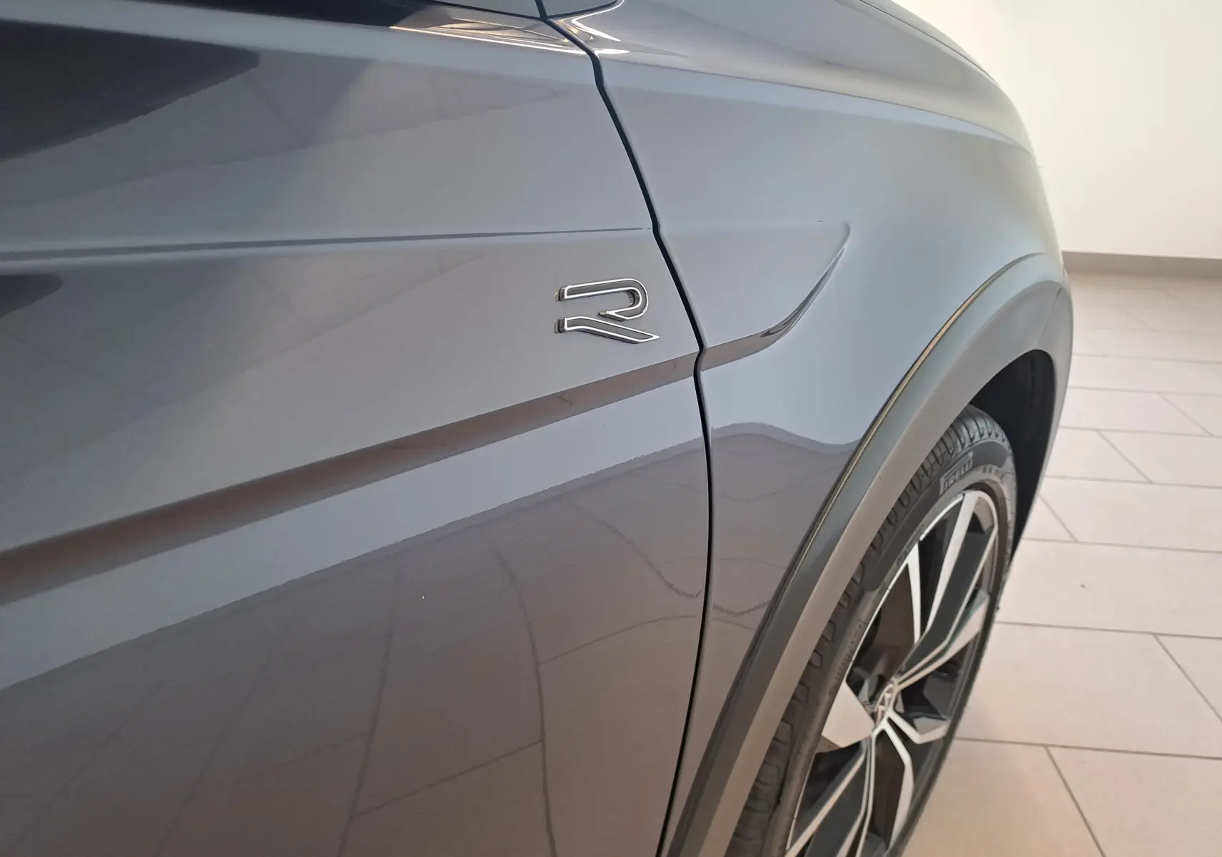 Gros plan sur l'aile avant droite gris cendre du Volkswagen Taigo 1.0 TSI R-Line avec logo "R" et jante alliage 18 pouces.