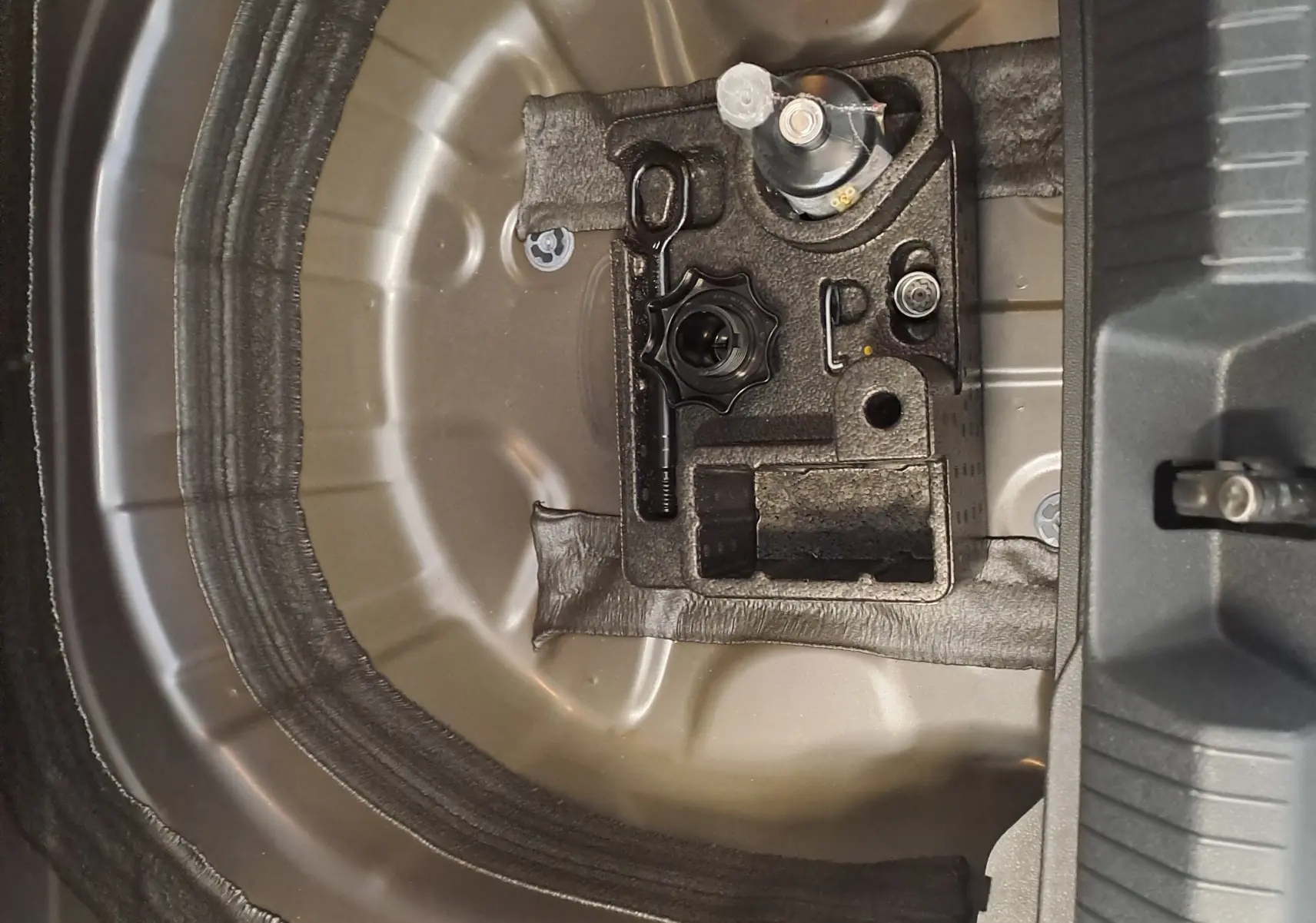 Vue rapprochée de la zone de rangement sous le coffre du Volkswagen Taigo gris cendre, montrant l'emplacement pour roue de secours.
