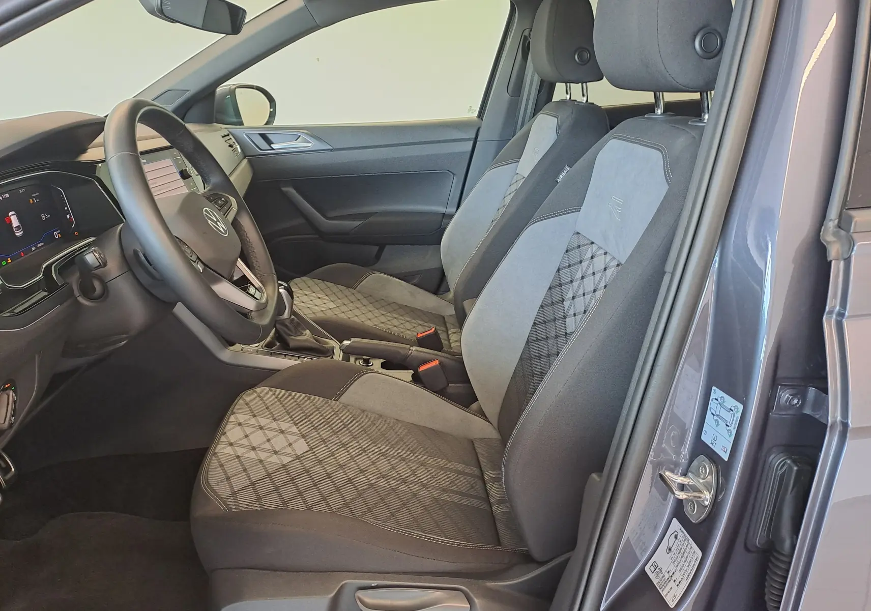 Vue intérieure côté conducteur de la Volkswagen Taigo gris cendre 2025, sièges tissu avec motifs géométriques et volant multifonction.
