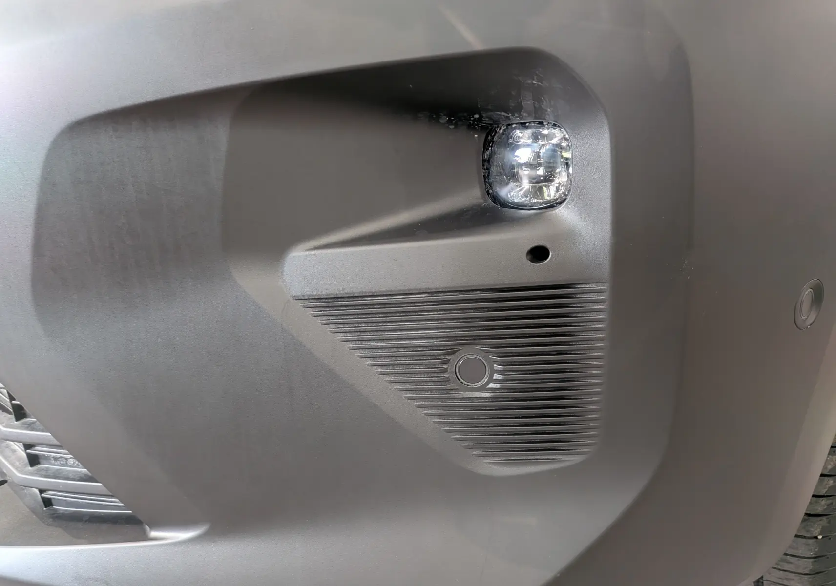 Gros plan sur le pare-chocs avant droit blanc du Citroën Berlingo 2025 avec antibrouillard et capteur de stationnement.