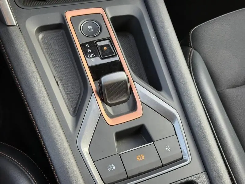 Gros plan sur la console centrale de la SEAT LEON 1.5 eTSI Hybrid 2025 avec levier de vitesses automatique et cadre cuivré.