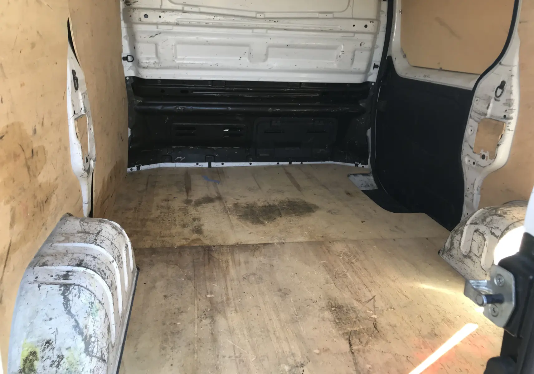 Intérieur du fourgon Renault Trafic blanc vu de l'arrière, montrant la zone de chargement avec revêtement en bois usé.