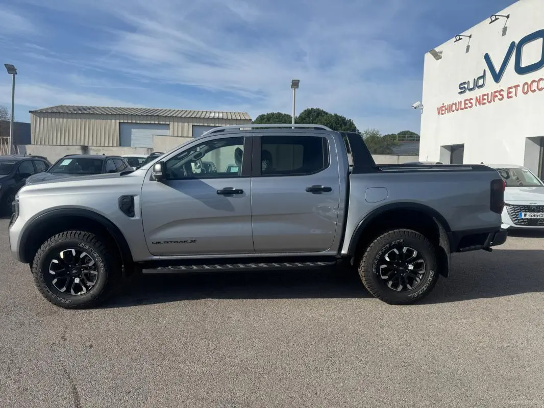 Vue de profil côté gauche d'un Ford Ranger gris 2025 Wildtrak X avec jantes alliage noires et barres de toit.