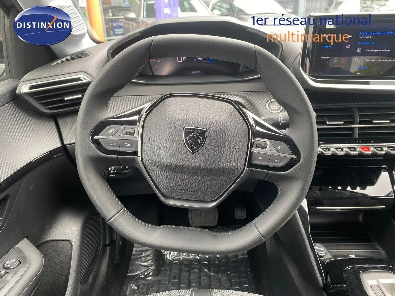 Vue intérieure centrée sur le volant cuir noir de la Peugeot 208 Hybrid 145ch avec tableau de bord et écran tactile.