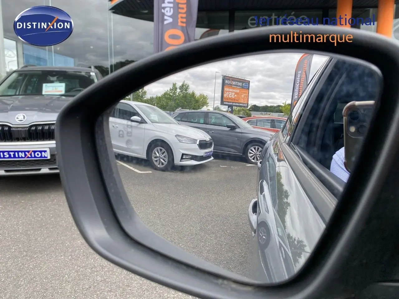 Rétroviseur droit montrant la Peugeot 208 Hybrid gris selenium métal vue de côté droit sur un parking multimarque.
