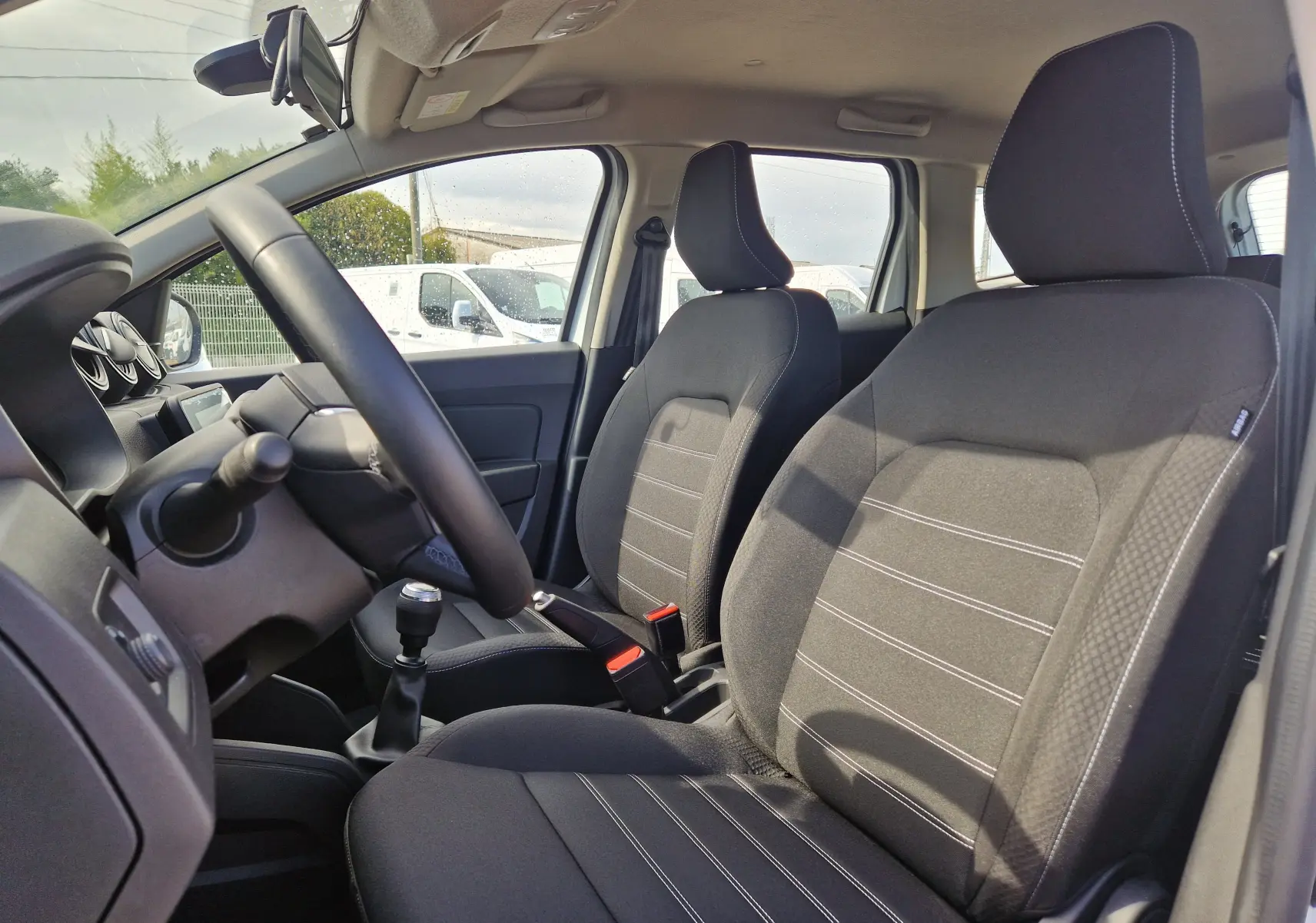 Vue intérieure côté conducteur du Dacia Duster 2023, sièges noirs avec coutures blanches et levier de vitesses manuel.