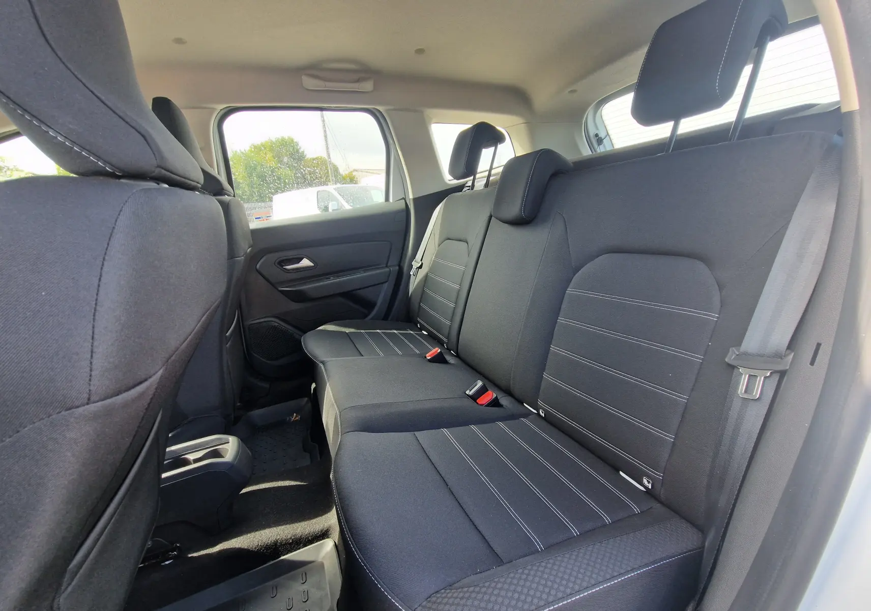 Vue intérieure côté droit des sièges arrière noirs du Dacia Duster 4x4 blanc, avec appuie-têtes et ceinture de sécurité visible.