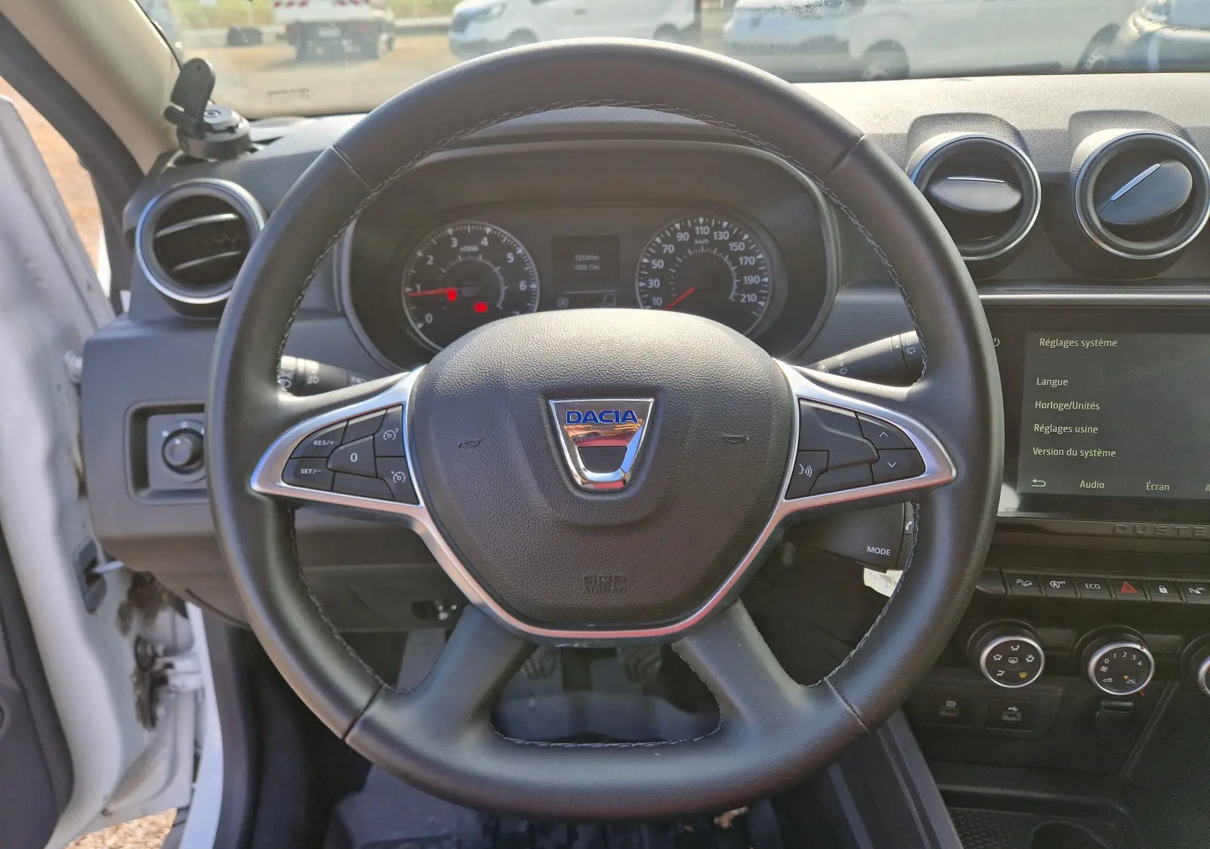 Vue intérieure centrée sur le volant noir du Dacia Duster 2023 avec tableau de bord et écran tactile visibles.