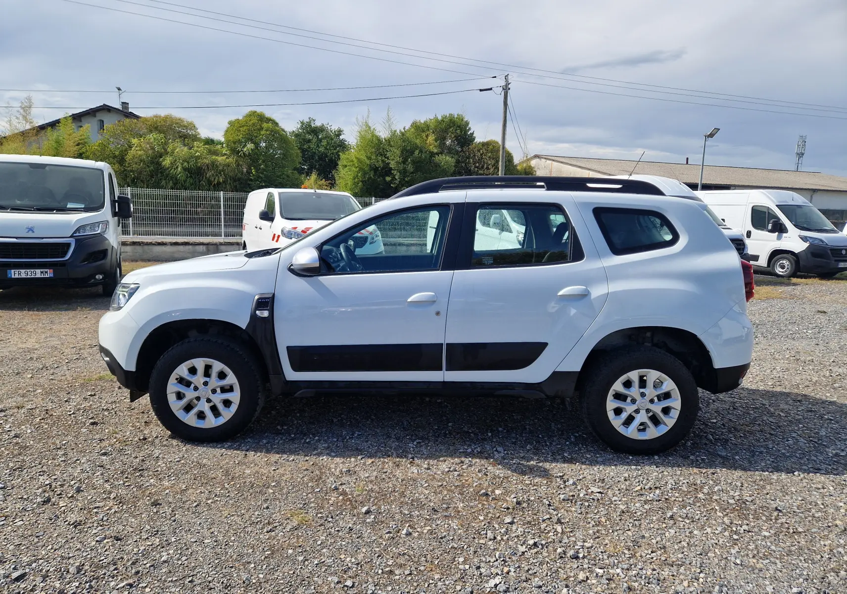 Dacia Duster blanc vue de profil côté gauche, SUV 4x4 avec protections noires et jantes alliage 16 pouces.
