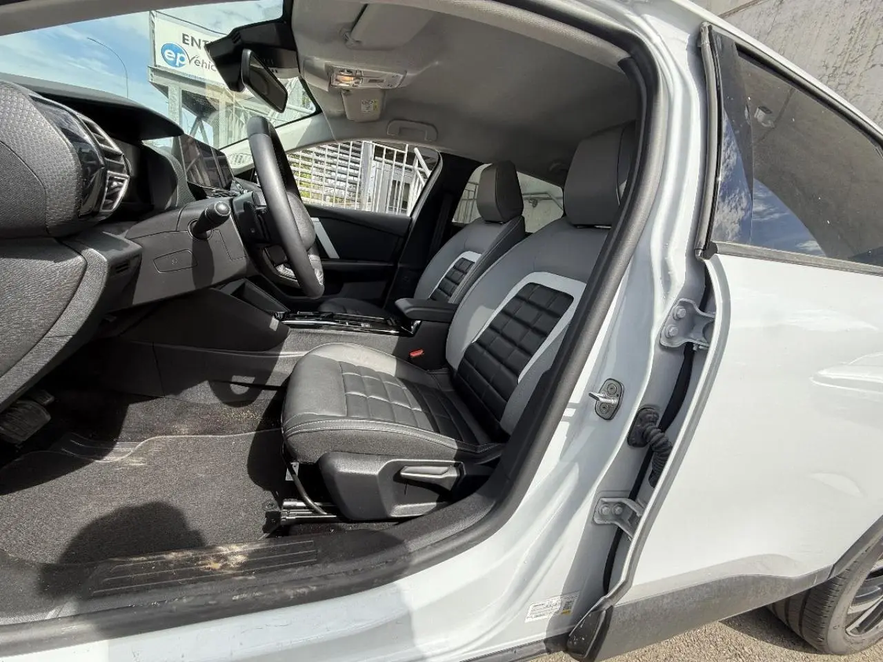 Vue côté conducteur intérieur de la Citroën C4 blanc okenite 2025, sièges bi-matière noirs et gris avec console centrale visible.