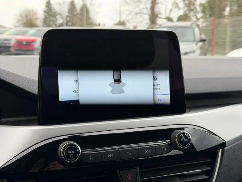 Vue intérieure du tableau de bord du Ford Kuga 2024, écran tactile central avec commandes audio et volume.