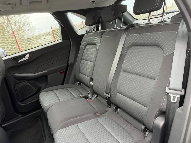 Vue intérieure du siège arrière côté gauche du Ford Kuga 2024, avec sellerie tissu gris à motifs et ceintures de sécurité visibles.