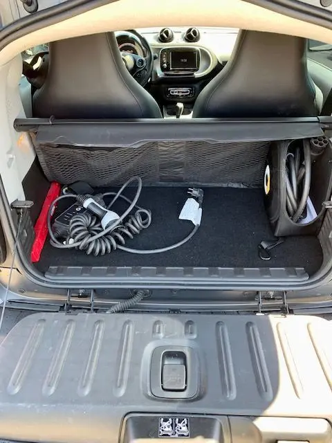 Coffre ouvert d'une Smart Fortwo électrique grise 2019, vue arrière montrant câbles de recharge et intérieur noir.