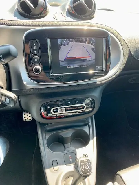Vue intérieure du tableau de bord et console centrale d'une Smart Fortwo électrique grise, avec écran de recul et levier de vitesses Brabus.