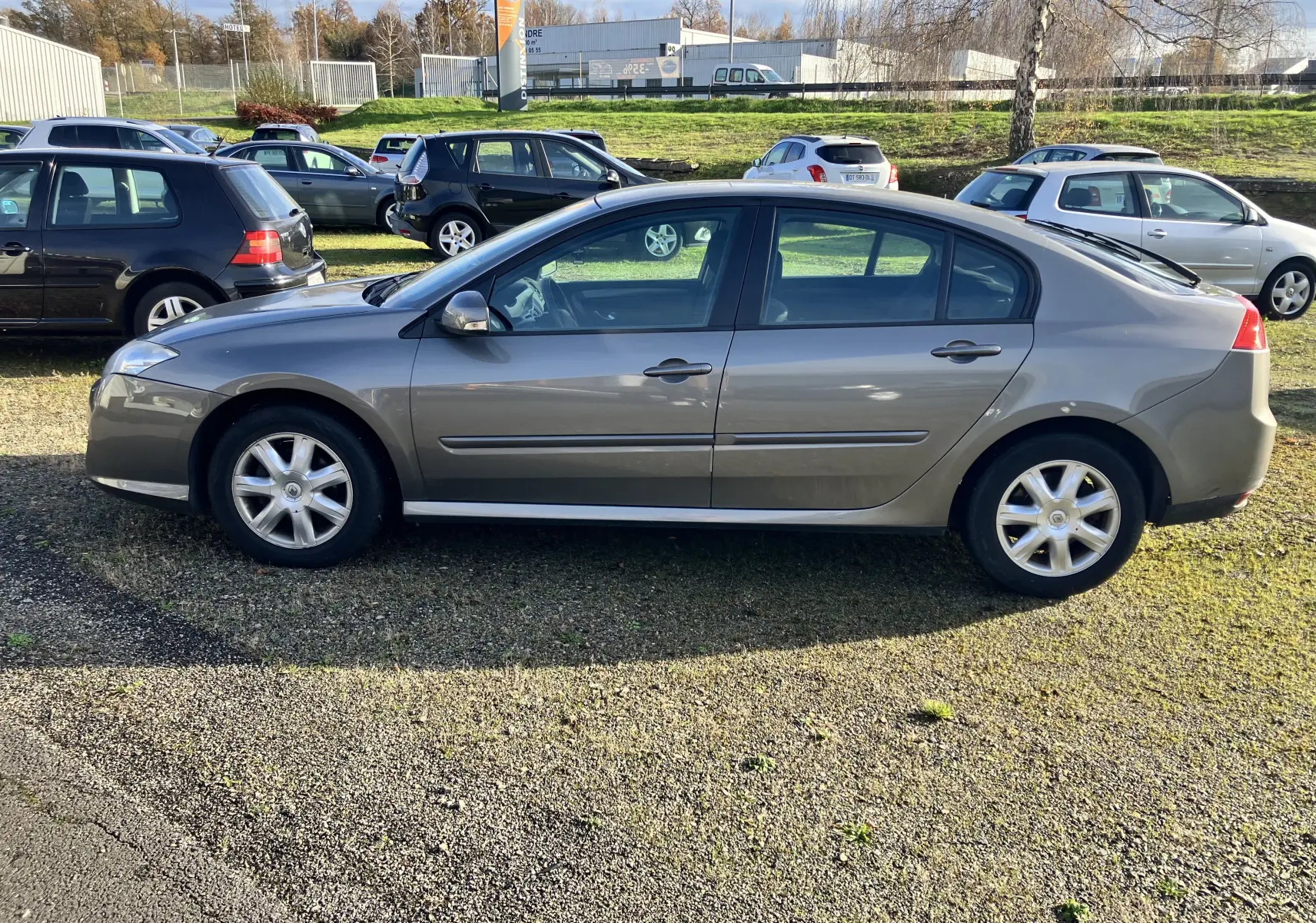 Profil côté gauche d'une Renault Laguna gris vert de 2008, berline 5 portes avec jantes alliage et vitres teintées.