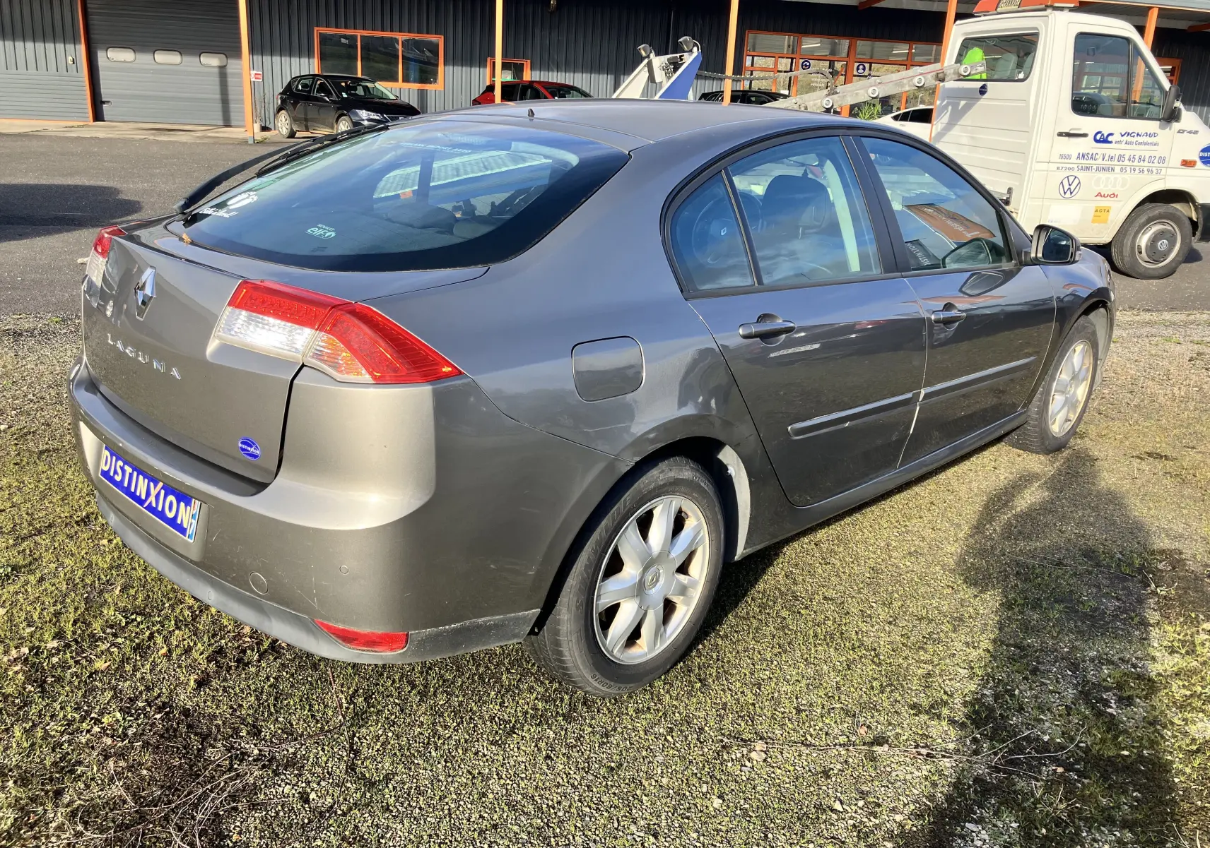 Renault Laguna 1.5l dCi 110 ch gris vert vue 3/4 arrière droit, berline 5 portes avec jantes alliage et feux arrière distinctifs.